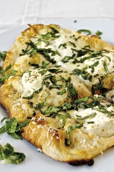 a white plate topped with a pizza covered in cheese and herbs on top of it