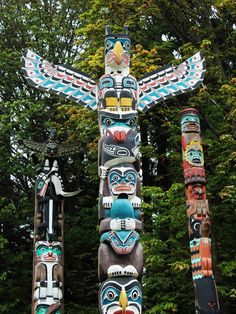 totems are lined up in the woods with trees behind them and one bird is perched on top