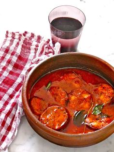 a wooden bowl filled with stew next to a red and white checkered napkin on top of a table