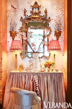 an ornate mirror is above a table with two lamps and a chair in front of it