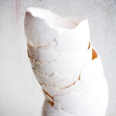 a white vase sitting on top of a table filled with lots of broken pieces of paper