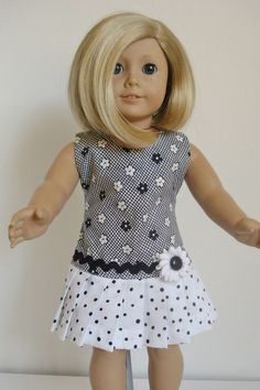 a doll with blonde hair wearing a black and white polka dot dress, holding her arms out