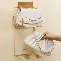 a hand holding a white purse next to a gold rack with two bags on it