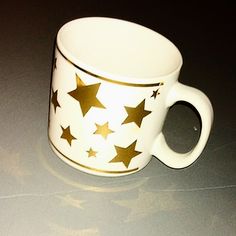 a white coffee cup with gold stars painted on the outside and inside, sitting on a table