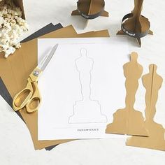 paper cutouts and scissors are sitting on top of some crafting supplies that include an oscar statue