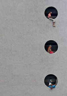 three round holes in the side of a building with people walking around them and one person on a skateboard