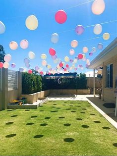 some balloons are floating in the air over a yard with grass and lawn furniture on it