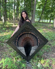 a woman standing in the middle of a forest holding up a large piece of art