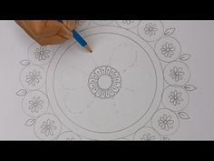 someone is drawing a flower design on paper with a marker and pencil, while another hand holds