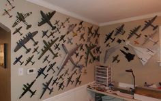 many model airplanes are hanging on the wall above a desk in a room with white walls