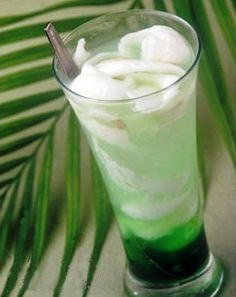 there is a green drink with ice in the glass on the table next to palm leaves