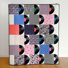 a colorful quilt is displayed on a wooden table with white wall in the back ground