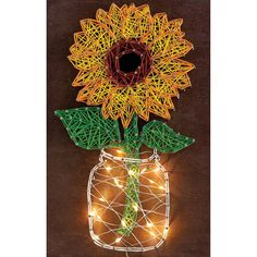 a string art sunflower in a mason jar with fairy lights on the outside and inside