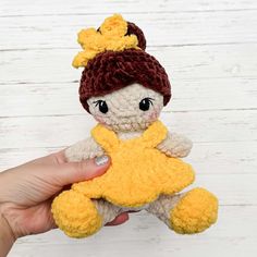 a hand holding a small yellow and brown teddy bear with a crochet hat