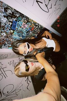 two women standing next to each other in front of graffiti covered walls