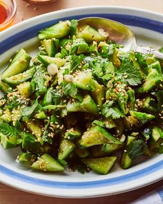 a white and blue plate topped with cucumber salad next to a cup of sauce