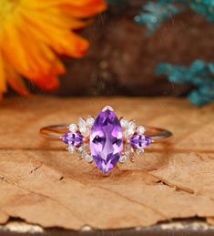 an amethorate and diamond ring sitting on top of a wooden table next to flowers