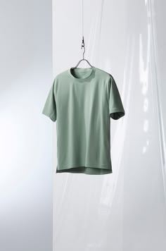 a green t - shirt hanging on a clothes line in front of a white wall