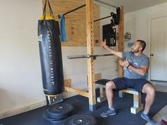 a man squats on a bench in front of a punching bag while holding a bar