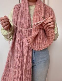 a woman wearing a pink knitted scarf and holding a pair of knitting needles in her hands