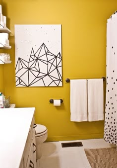 a bathroom with yellow walls and black and white artwork on the wall above the toilet