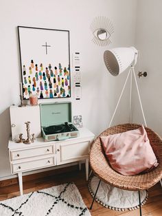 a room with a wicker chair, white table and art on the wall above it