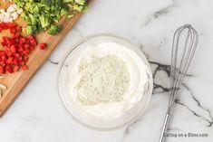 a cutting board topped with vegetables next to a whisk and some other ingredients