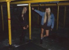 two young women standing next to each other under a yellow and black structure in the dark