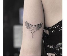 a woman's arm with a cross and wings tattoo on the left side of her arm