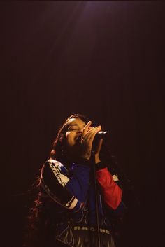 a woman singing into a microphone while standing in front of a dark stage with lights