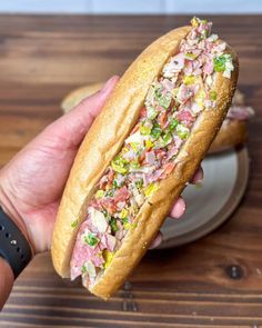 a hand holding a sandwich with meat and veggies in it on a plate