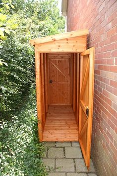 a small wooden outhouse sitting next to a brick wall and green bushes in the background