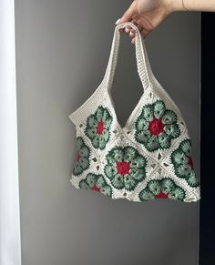 a crocheted bag hanging on the wall with a hand holding it up to its side