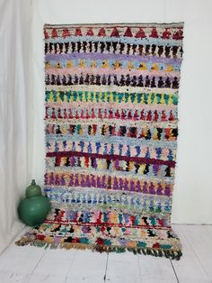 a large multicolored rug on the floor next to a green vase and white wall