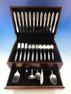 an assortment of silverware is displayed in a wooden display case on a blue background