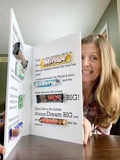 a woman sitting at a table holding up an open book with candy bars on it