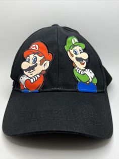 🔥🔥BRAND NEW WITH ORIGINAL TAGS NEVER WORN🔥🔥Show off your love for the iconic video game duo with this Super Mario Luigi Official Nintendo 2012 Black Strap Back Lid Cap. Made from 100% cotton and in a classic denim fabric type, this trucker hat is perfect for any season. The adjustable strap ensures a comfortable fit for any head size and the vintage design adds a touch of nostalgia. Featuring the colorful and classic characters of Mario and Luigi, this hat is a must-have for any gamer or fan Fun Black Cotton Baseball Cap, Retro Black Cotton Baseball Cap, Retro Baseball Cap With Graphic Print, Retro Black Baseball Cap With Embroidered Logo, Black Novelty Cotton Hat, Super Mario And Luigi, Mario And Luigi, Denim Fabric, Super Mario