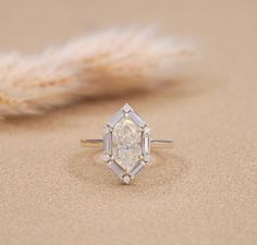 a diamond ring sitting on top of a sandy beach next to a feathery plant