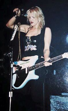 a woman holding a white guitar while standing on top of a stage in front of a microphone