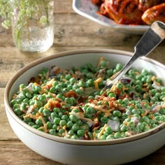 a bowl filled with peas and meat on top of a wooden table next to a plate of chicken wings