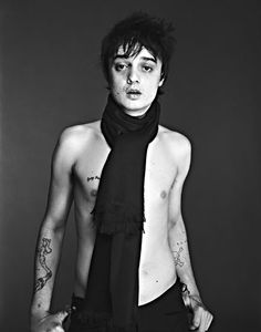 black and white photograph of a shirtless man with tattoos on his chest wearing a scarf