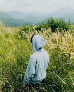 a person in a blue hoodie standing in tall grass with mountains in the background