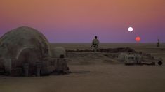 a man standing on top of a sandy field next to a large object in the distance