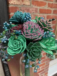 a vase filled with green and pink flowers on top of a table next to a brick wall