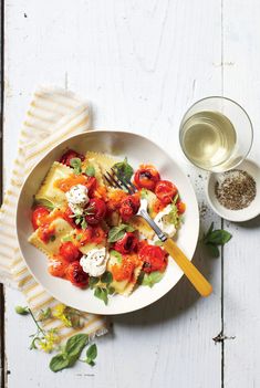 a white plate topped with pasta and tomatoes next to a glass of water on top of a wooden table