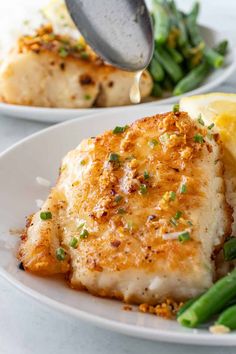 a white plate topped with fish and asparagus covered in gravy next to a lemon wedge