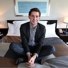 a man sitting on top of a bed in a bedroom next to two lamps and a painting