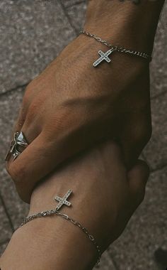 two people holding hands with cross bracelets on their wrists and one wearing a ring