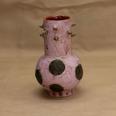 a pink vase with green polka dots and rivets on the outside, sitting on a tan surface