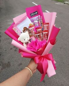 a person is holding a pink bouquet with candy and a teddy bear in the center